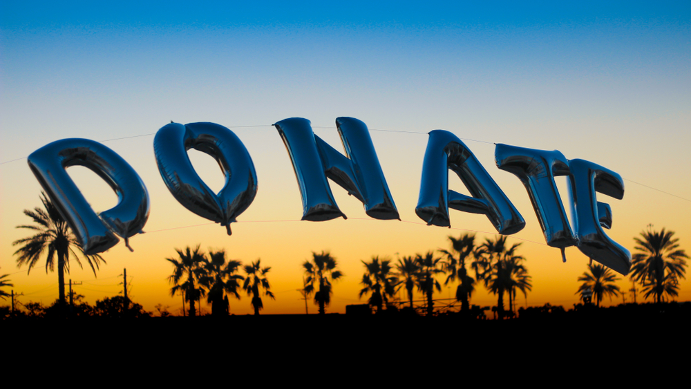 "Donate" Spelled out in balloons with palm trees in the background at sunset.